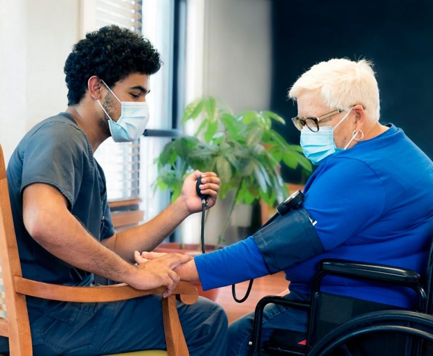 un infirmier en train de prendre la tension d'une patiente âgée en fauteuil roulant